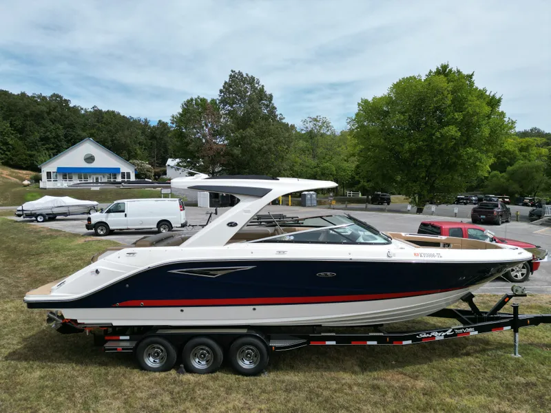 Slide: The Image of 2022 Sea Ray SLX 310 boat on trailer, parked outdoors near trees and vehicles. - 1