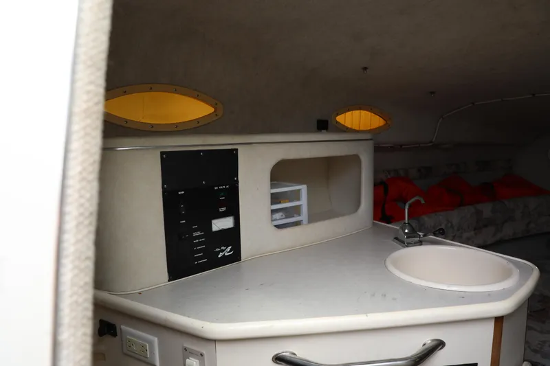 Slide: The Image of Interior of a 1998 Searay Sundancer boat featuring a compact kitchenette and cozy seating area. - 12