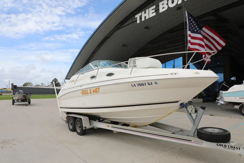 Slide: The Image of 1998 Searay Sundancer boat on trailer with American flag, parked outside a building. - 2