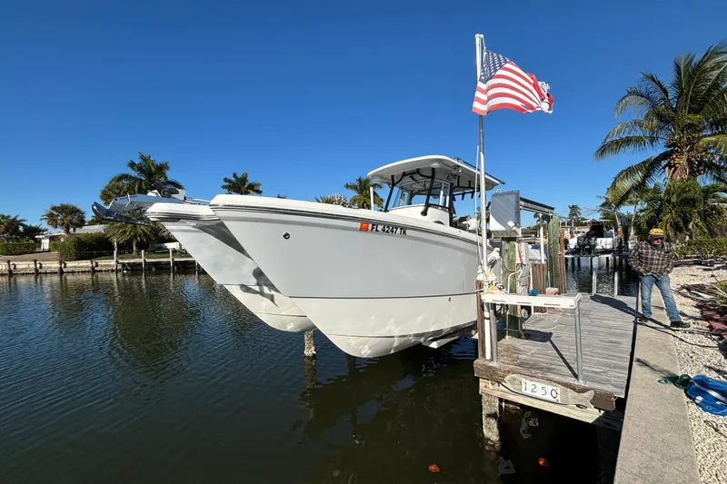 The Image of 2023 World Cat 295 CC boat docked with American flag, clear sky, and palm trees. - 1