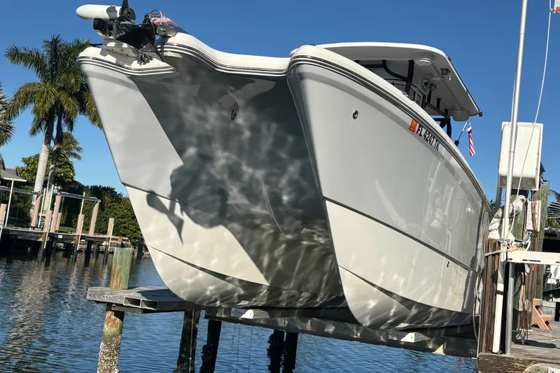 Slide: The Image of 2023 World Cat 295 CC boat on lift, reflecting sunlight, with palm trees in background. - 10