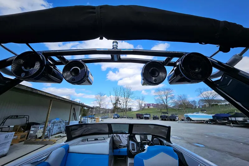 Slide: The Image of 2022 Supreme S220 boat with speakers and blue seating, parked outdoors under a clear sky. - 15