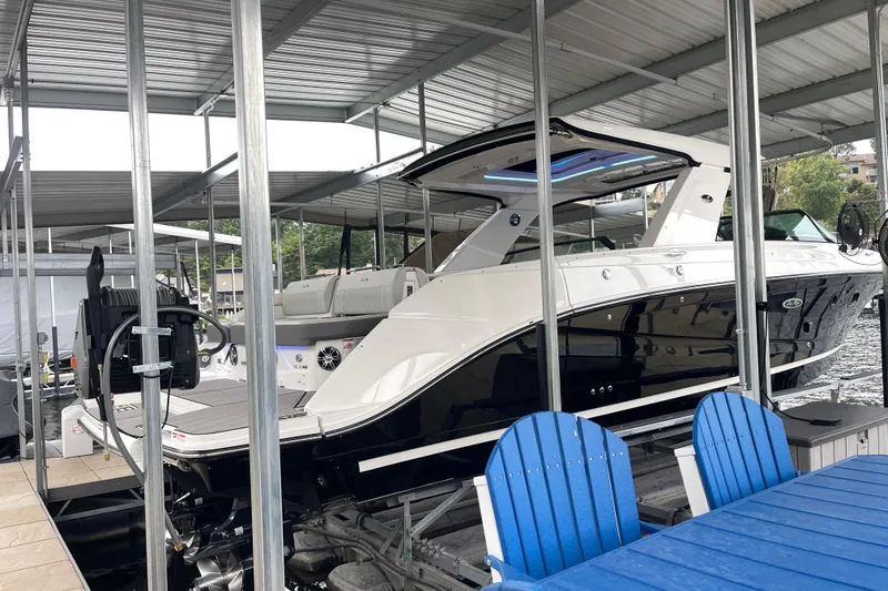 Slide: The Image of 2023 Sea Ray SLX 400 boat docked under a covered marina with blue chairs nearby. - 8