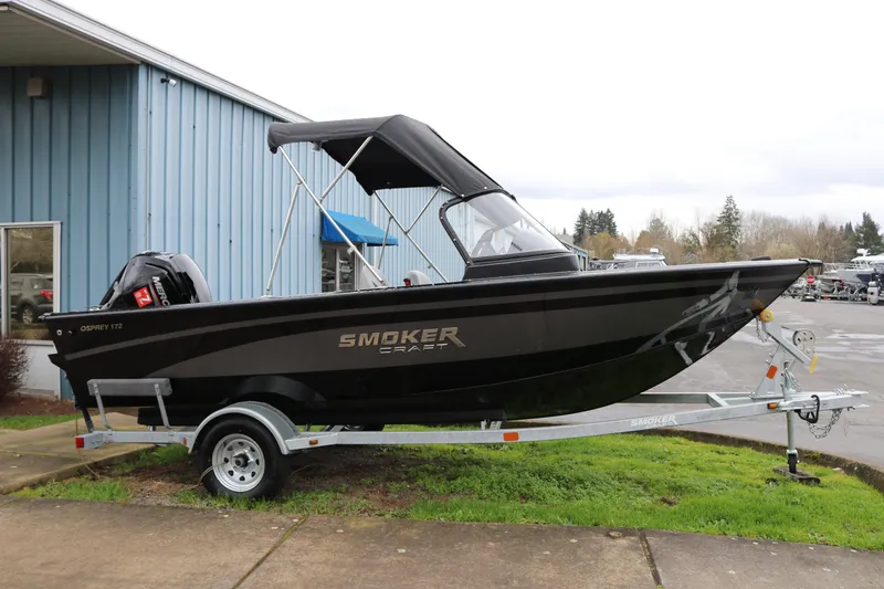 Slide: The Image of 2026 Smoker Craft Osprey 172 boat on trailer, parked outside a blue building. - 3
