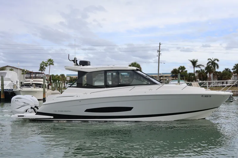 Slide: The Image of 2022 Regal 36 XO boat cruising on a calm waterway with palm trees in the background. - 1