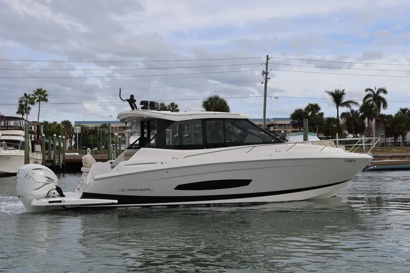 Slide: The Image of 2022 Regal 36 XO boat cruising on a calm waterway with palm trees in the background. - 5