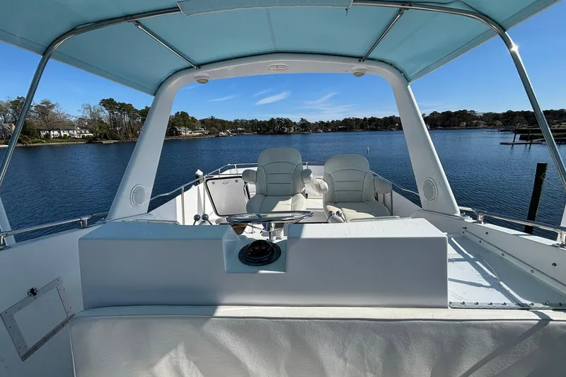 Slide: The Image of 1979 Hatteras 53 Motor Yacht helm with white seating, overlooking serene water and shoreline. - 44