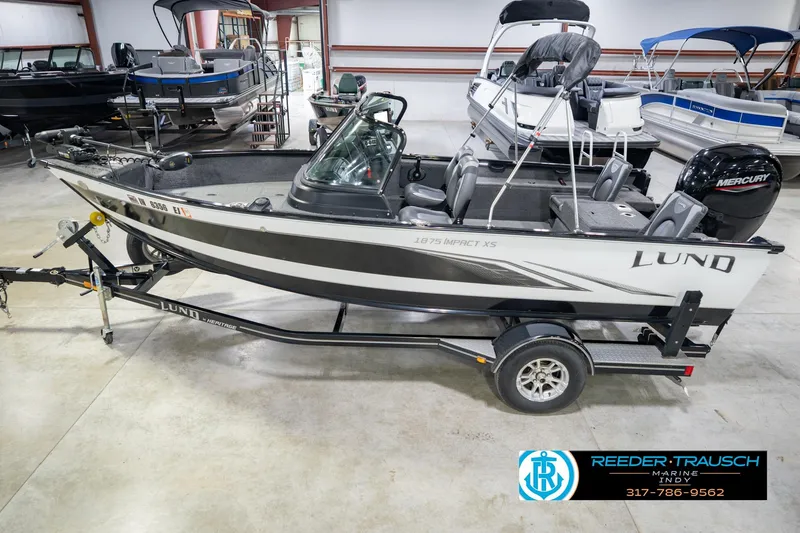 The Image of 2022 Lund 1875 Impact boat on trailer in showroom, featuring Mercury engine. - 2
