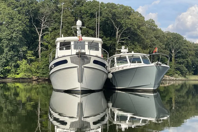 Slide: The Image of Two boats, including a 2008 Nordic Tug 42, reflected on calm water near a forested shoreline. - 4