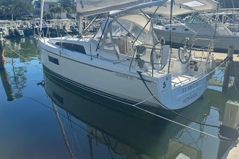 Slide: The Image of 2020 Beneteau Oceanis 30.1 sailboat docked in a marina, reflecting on calm water. - 1