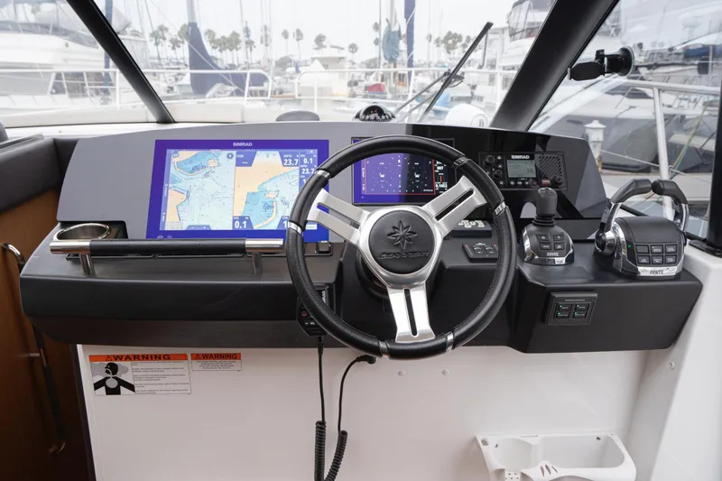 Slide: The Image of 2014 Jeanneau NC 14 helm with navigation screens and controls in a marina setting. - 26