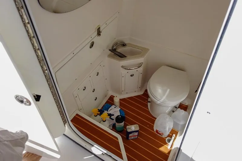 Slide: The Image of 2015 Edgewater 320CC boat bathroom with sink, toilet, and cleaning supplies on wooden floor. - 18