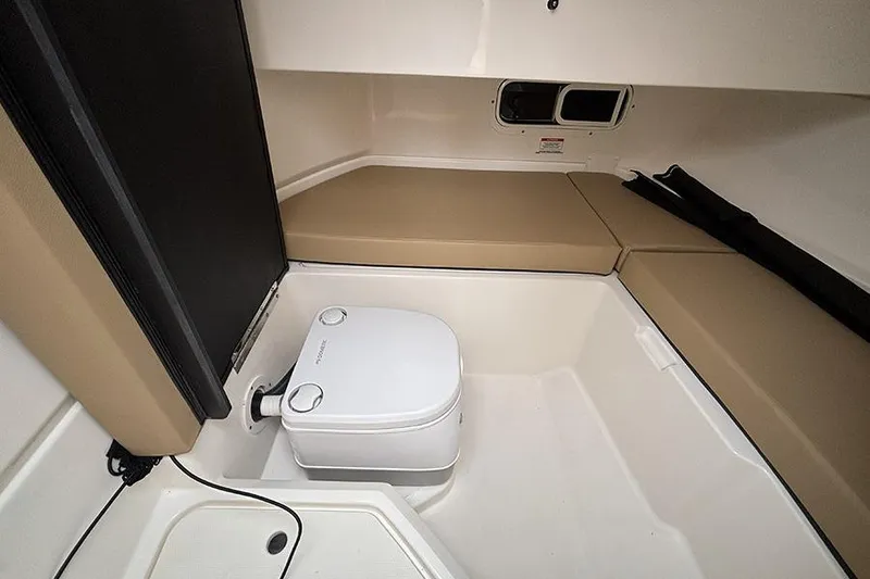 Slide: The Image of 2024 Sea Ray SDX 250 cabin interior with portable toilet and cushioned seating. - 25