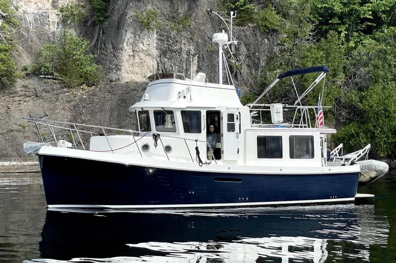 The Image of 2007 American Tug 34 boat on calm water near rocky shoreline. - 0