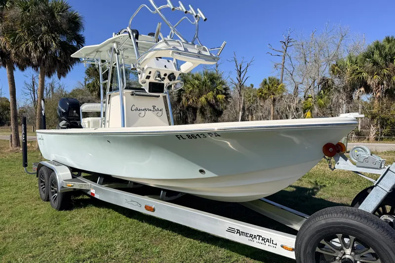 Slide: The Image of 2010 Canyon Bay 24H boat on trailer, parked on grass with palm trees in background. - 2