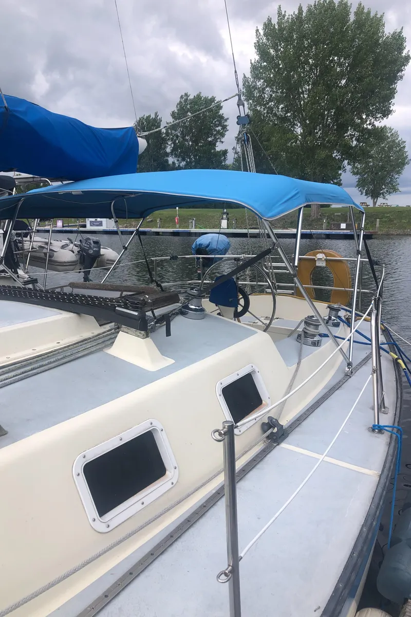 Slide: The Image of 1980 Lancer 36 sailboat with blue canopy docked by a tree-lined shore. - 5