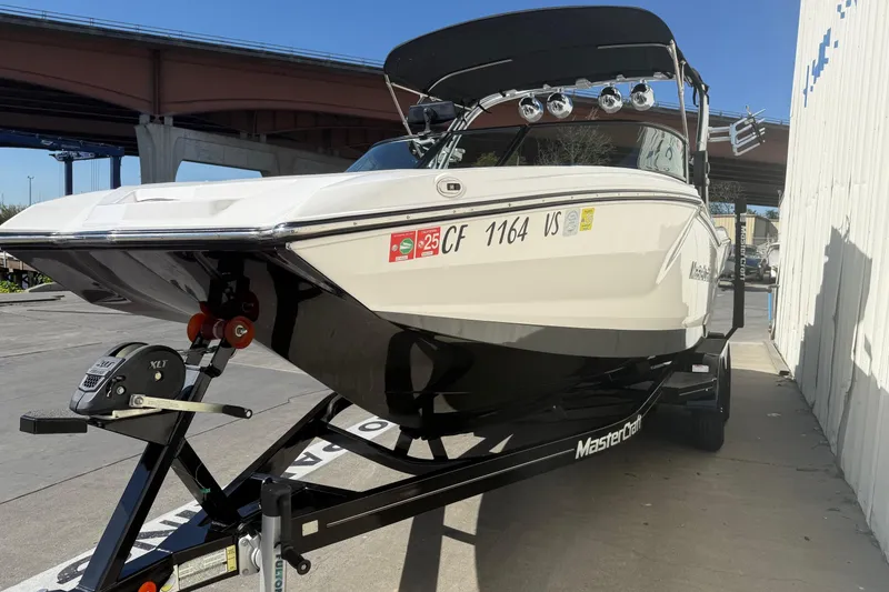Slide: The Image of 2020 MasterCraft NXT22 boat on trailer, parked outdoors under a bridge. - 3