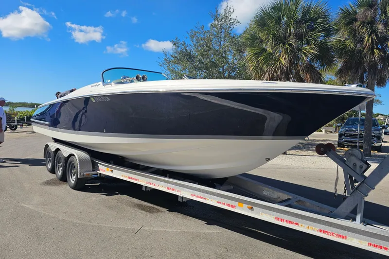 Slide: The Image of 2003 Chris-Craft Launch 28 boat on trailer, parked near palm trees under blue sky. - 15