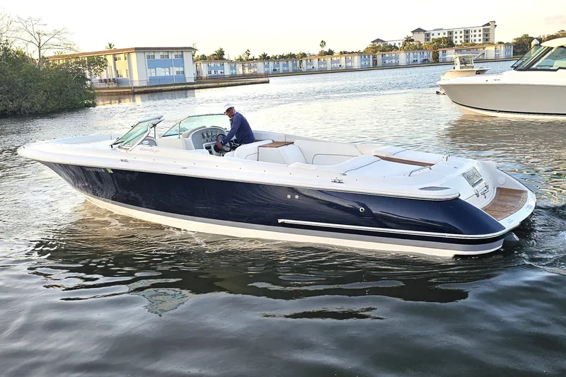 Slide: The Image of 2003 Chris-Craft Launch 28 boat cruising on calm waters near modern buildings. - 2