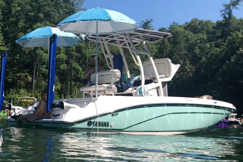 Slide: The Image of 2020 Yamaha Boats 195 FSH Sport on water, featuring blue umbrellas and lush forest backdrop. - 3
