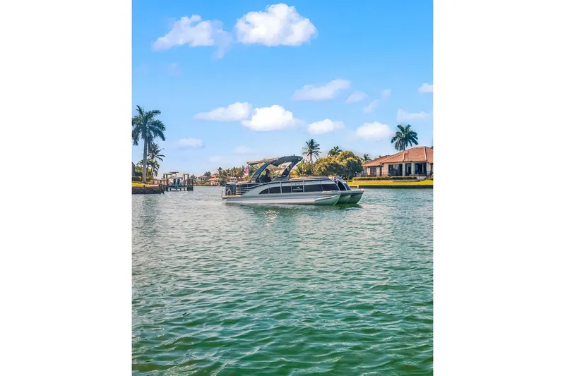 The Image of 2018 Bennington 25 QSR pontoon boat on a scenic waterway with palm trees and houses. - 0