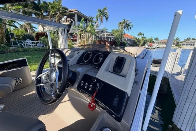 Slide: The Image of 2018 Bennington 25 QSR boat dashboard with steering wheel, docked by a scenic waterfront. - 20