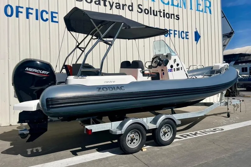 Slide: The Image of 2024 Zodiac Medline 6.8 boat on trailer, featuring Mercury outboard motor, parked outside office. - 7