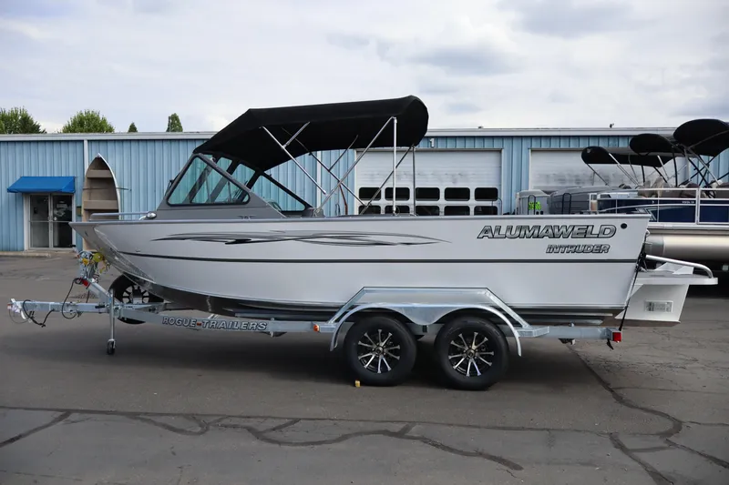 Slide: The Image of 2026 Alumaweld Intruder Outboard 20 boat on trailer, parked outside a blue building. - 4