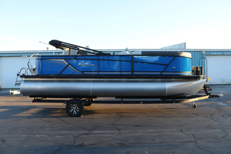 Slide: The Image of 2026 SunChaser Geneva Fish 22 pontoon boat on trailer, blue exterior, parked outdoors. - 6