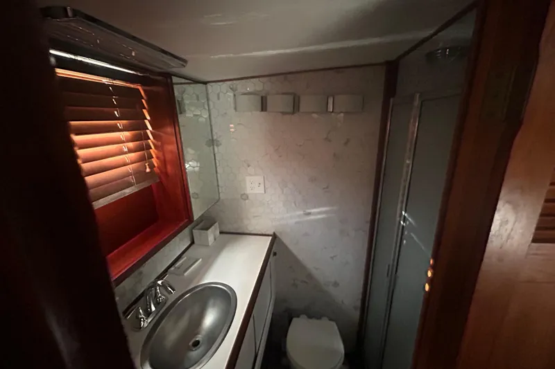 Slide: The Image of 1980 Trojan F44 yacht bathroom with sink, toilet, and shower, featuring wooden blinds and hexagonal tiles. - 8