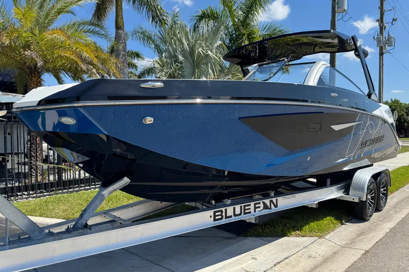Slide: The Image of 2022 Scarab 285 ID boat on trailer, parked near palm trees under a clear blue sky. - 20