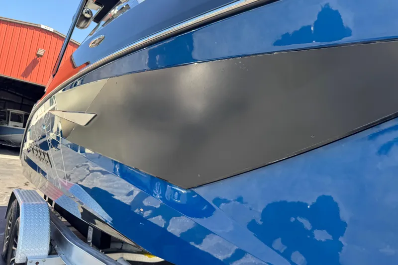 Slide: The Image of 2022 Scarab 285 ID boat in blue, parked on a trailer near a red building. - 93