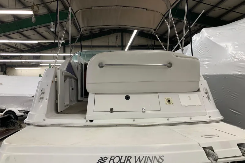 Slide: The Image of 2003 Four Winns 248 Vista boat interior, featuring rear seating and canopy in a warehouse setting. - 4