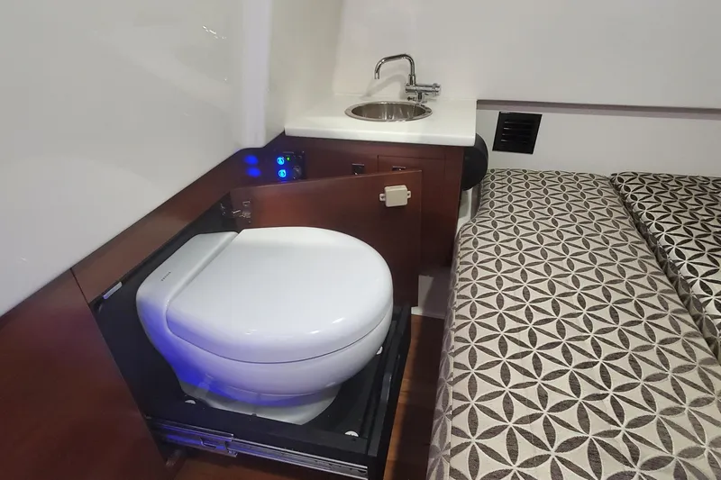 Slide: The Image of 2023 Chaparral 300 OSX cabin interior with toilet, sink, and patterned bedding. - 46