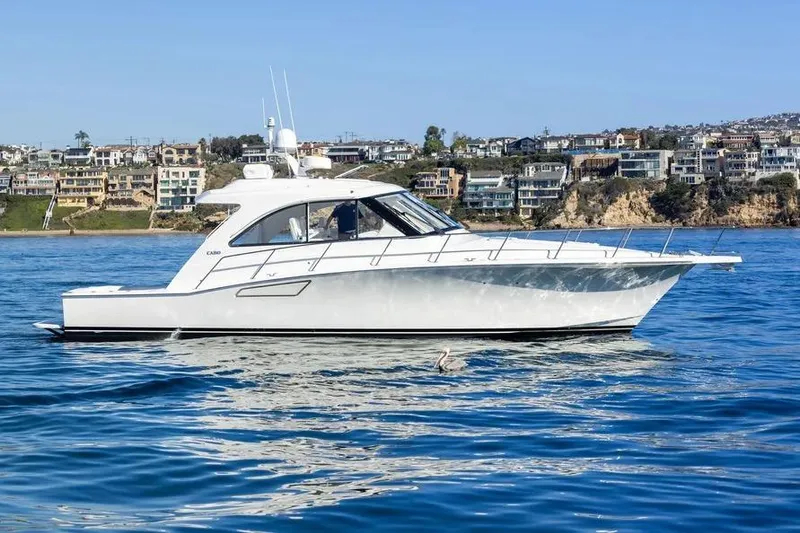 The Image of 2012 Cabo 44 Hardtop Express yacht cruising near coastal homes. - 1
