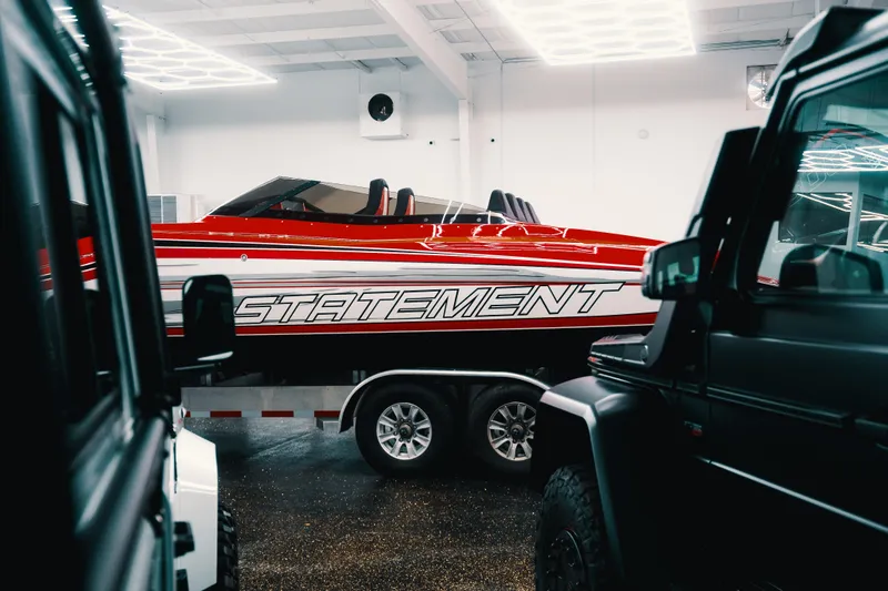 Slide: The Image of Red Statement 360 CAT boat on trailer in showroom, surrounded by vehicles. - 5