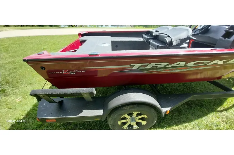 Slide: The Image of 2025 Tracker Super Guide V-16 SC boat on trailer, red exterior, parked on grass. - 23