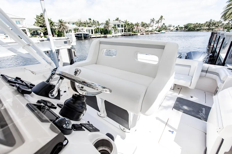 Slide: The Image of 2016 Intrepid 400 Cuddy boat interior with steering wheel and seating, docked by waterfront homes. - 3