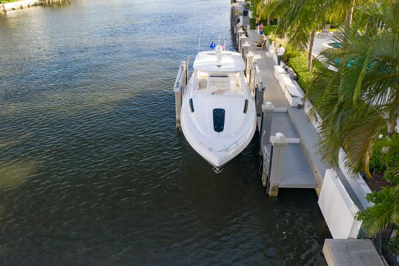 Slide: The Image of 2016 Intrepid 400 Cuddy yacht docked by a waterfront, surrounded by lush greenery. - 45