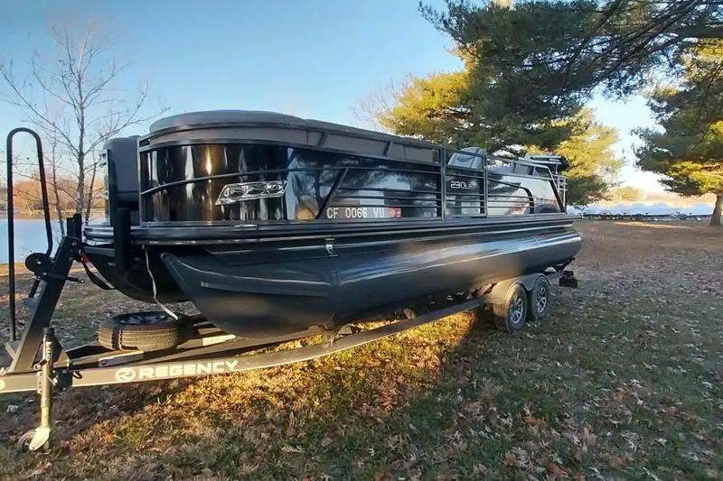 Slide: The Image of 2021 Regency 230 LE3 Sport pontoon boat on trailer, parked near a lake. - 10