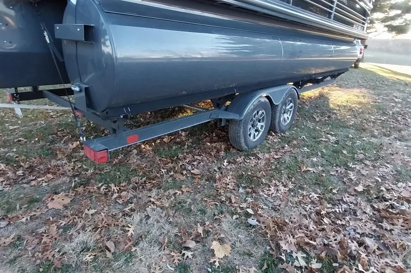 Slide: The Image of 2021 Regency 230 LE3 Sport pontoon trailer on grassy, leaf-covered ground. - 34