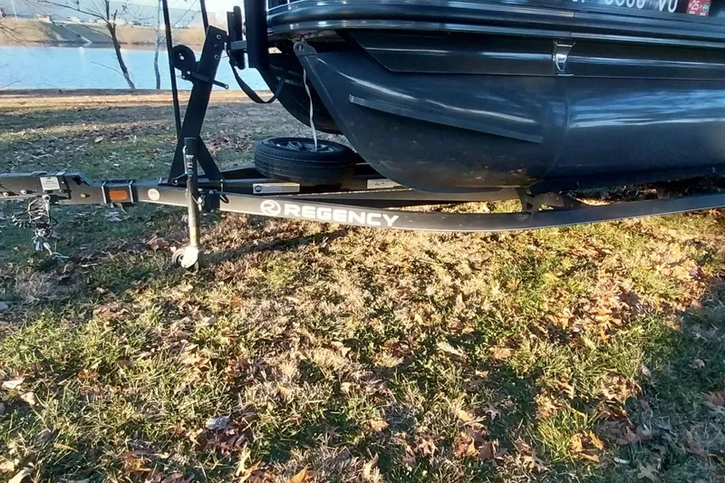 Slide: The Image of Trailer of 2021 Regency 230 LE3 Sport boat on grassy lakeside. - 5