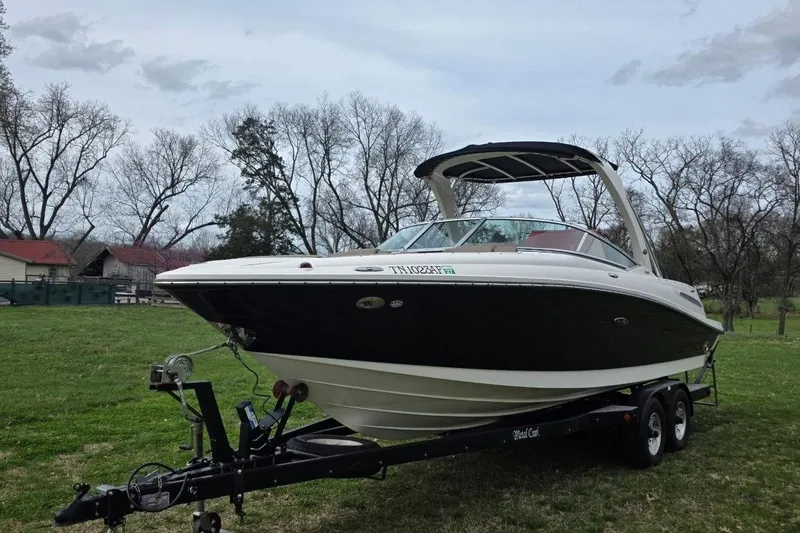 The Image of 2011 Sea Ray SLX 250 boat on trailer, parked on grassy area with trees in background. - 0