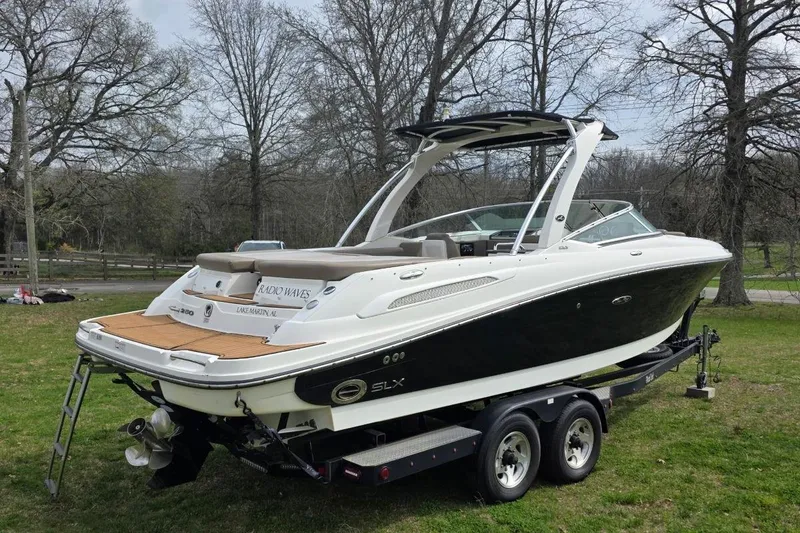 Slide: The Image of 2011 Sea Ray SLX 250 boat on trailer, parked on grass with trees in background. - 2