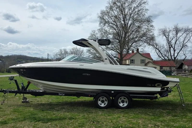 Slide: The Image of 2011 Sea Ray SLX 250 boat on trailer, parked on grass with trees and houses in background. - 6