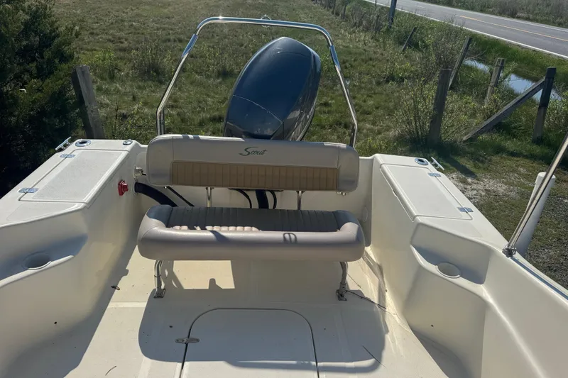 Slide: The Image of 2004 Scout 175 Dorado boat interior with seating and motor, parked near grassy area. - 12