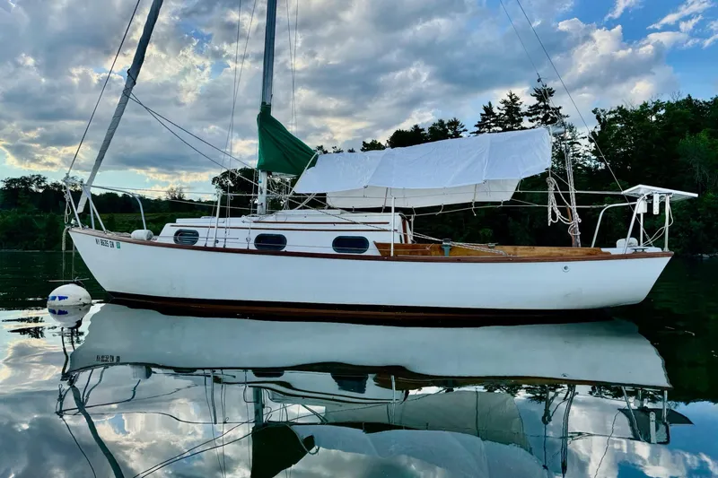Slide: The Image of 1981 Cape Dory 25 sailboat on calm water, surrounded by trees and a cloudy sky. - 3