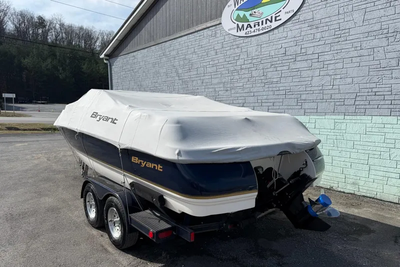 Slide: The Image of 1998 Bryant 214 Limited boat covered, parked on a trailer near a marine service building. - 13