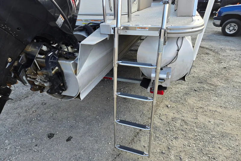 Slide: The Image of 2020 Avalon LSZ VRB 24' boat with ladder and motor, parked on gravel. - 18