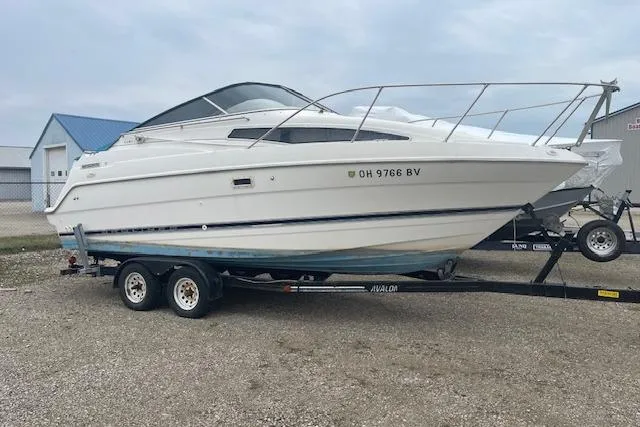 The Image of 1997 Bayliner 2355 boat on trailer, parked outdoors, with registration number visible. - 0